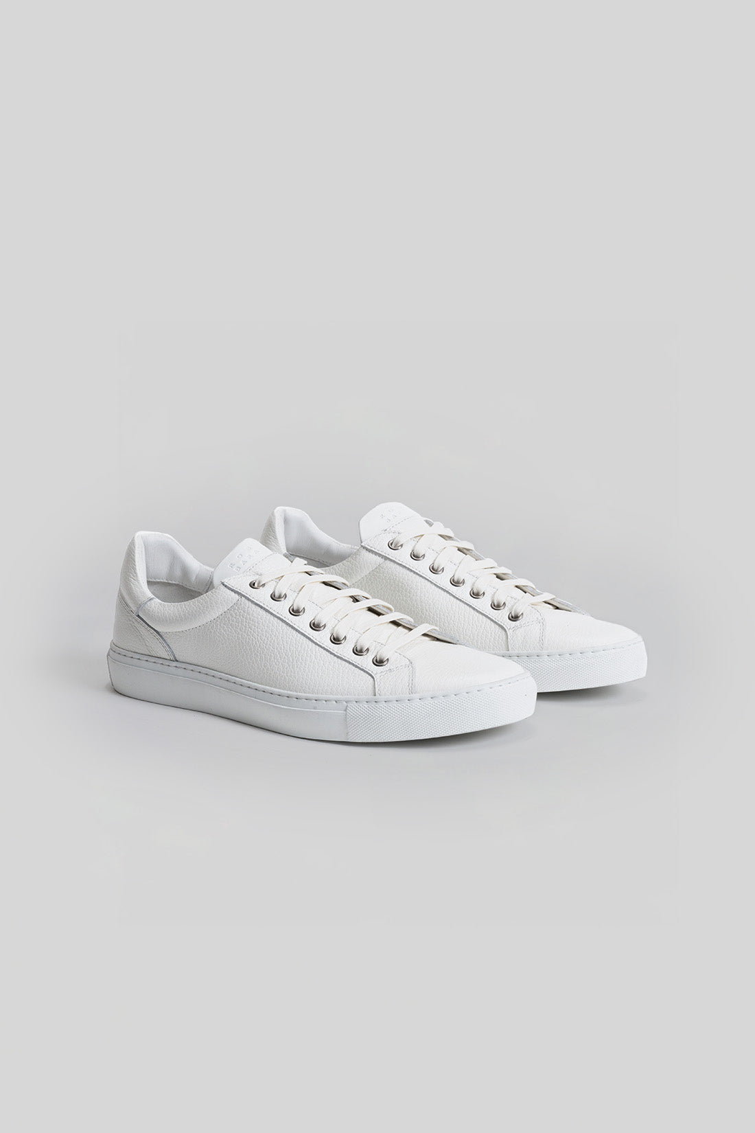 White lace-up sneakers with textured leather uppers and padded collars shown as a pair.