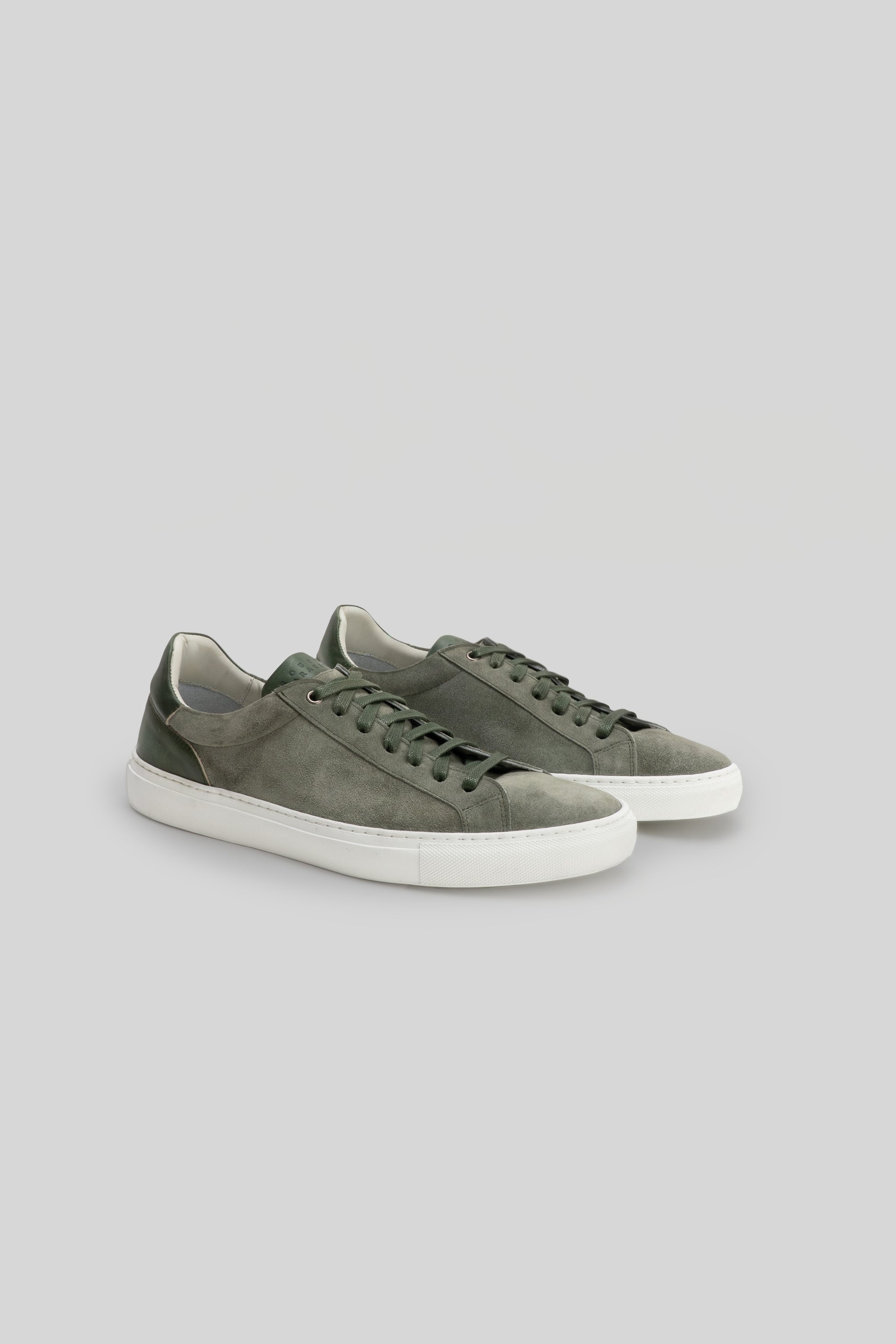 Olive green suede sneakers with white rubber sole and lace-up front closure.