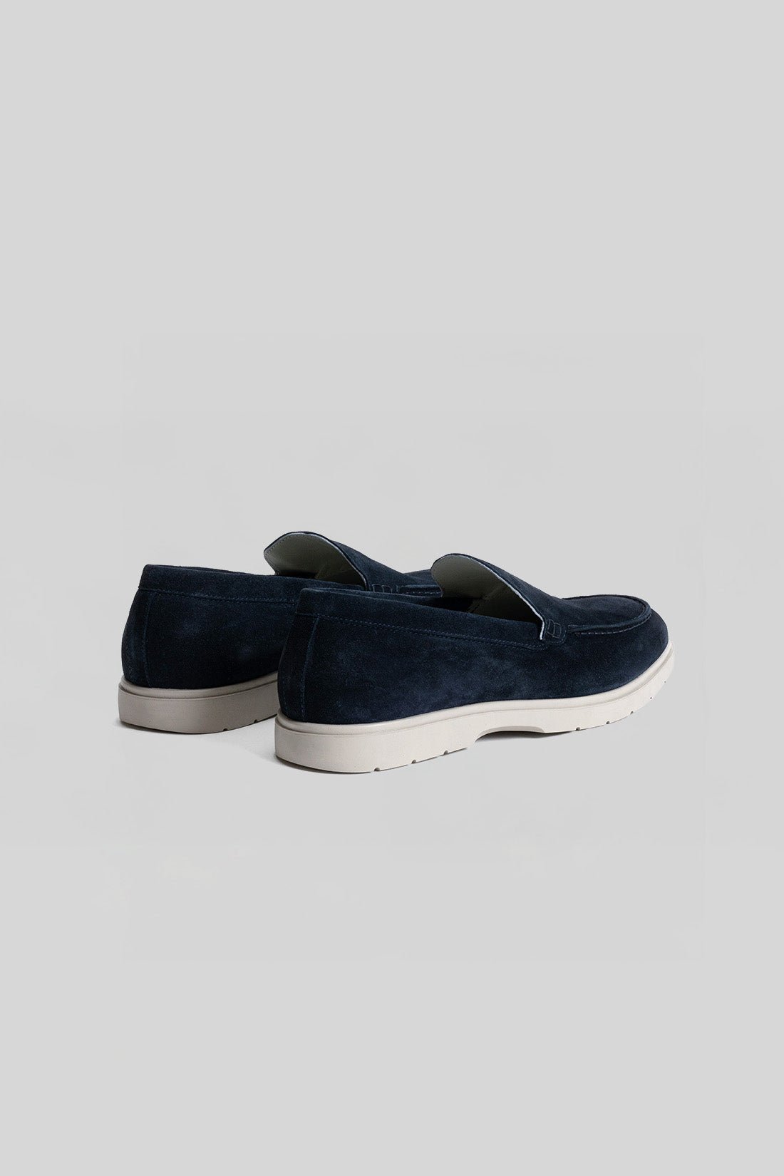 Navy suede loafers with white rubber sole and slip-on design, shown from the back.