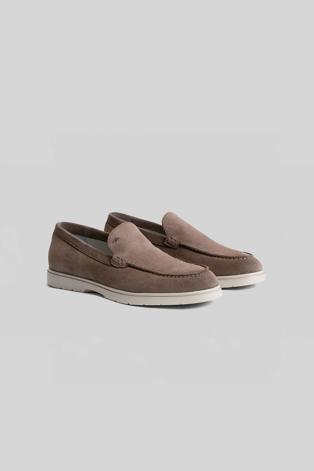 Pair of taupe suede loafers with white rubber soles and penny slot detailing on the vamp.