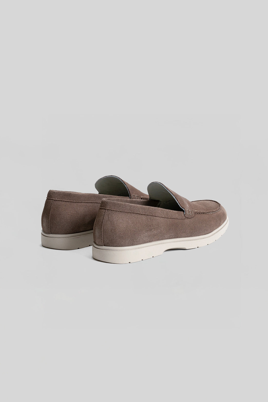 Brown suede loafers with white crepe soles, shown from rear three-quarter view.