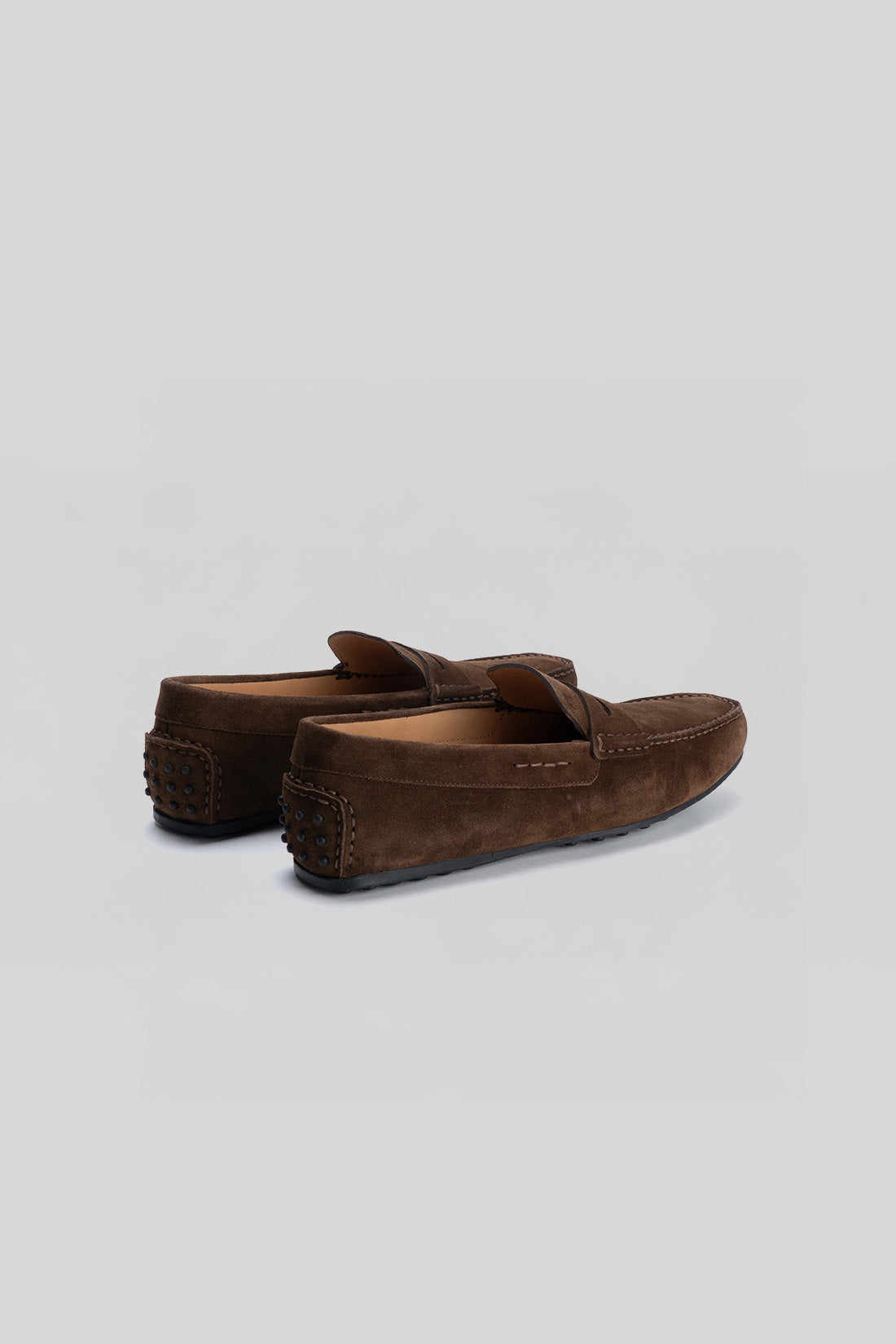 Pair of brown suede loafers with studded heel detail and tan leather interior, shown from the rear angle.