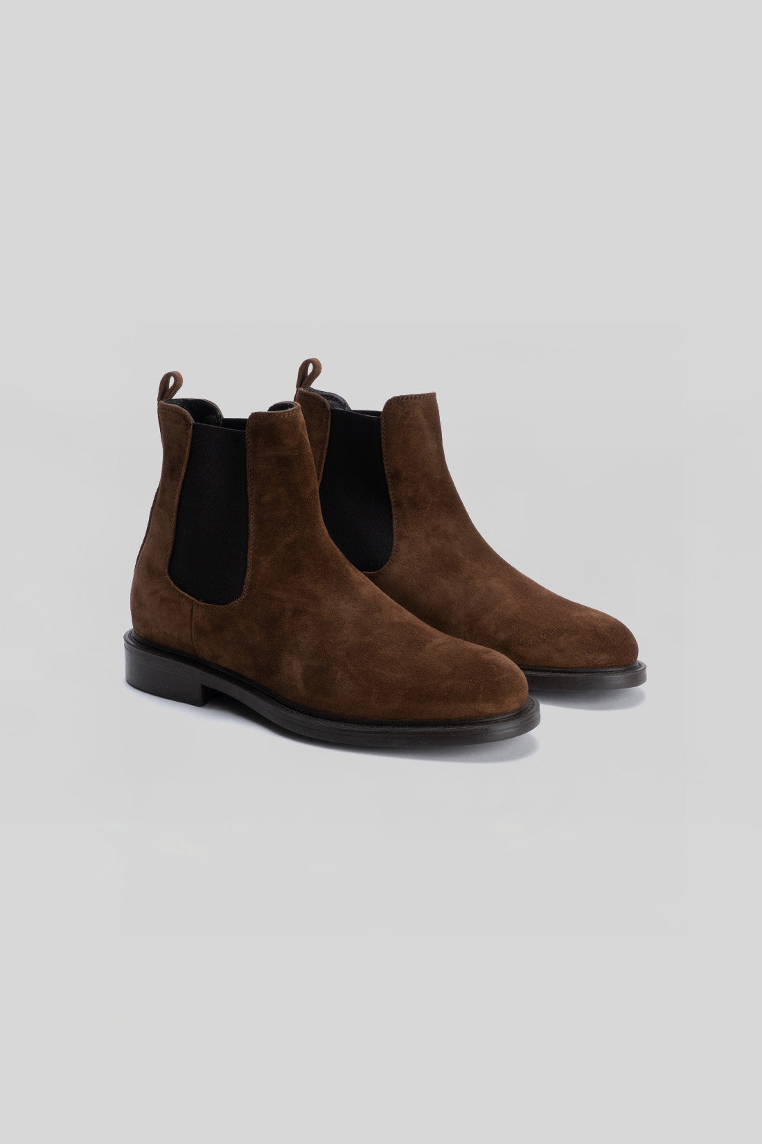 Brown suede Chelsea boots with black elastic side panels and black rubber soles, shown from a front angle.