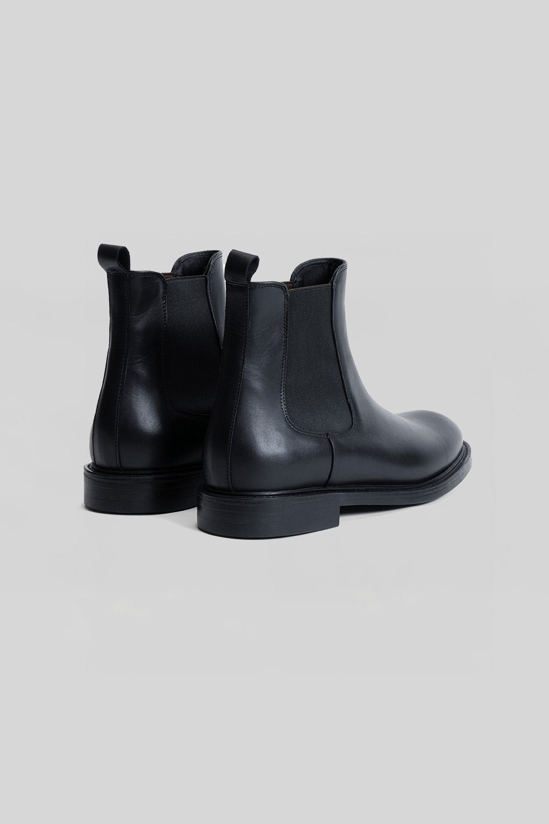 Black leather Chelsea boot with elastic side panels and chunky sole, shown from rear view.