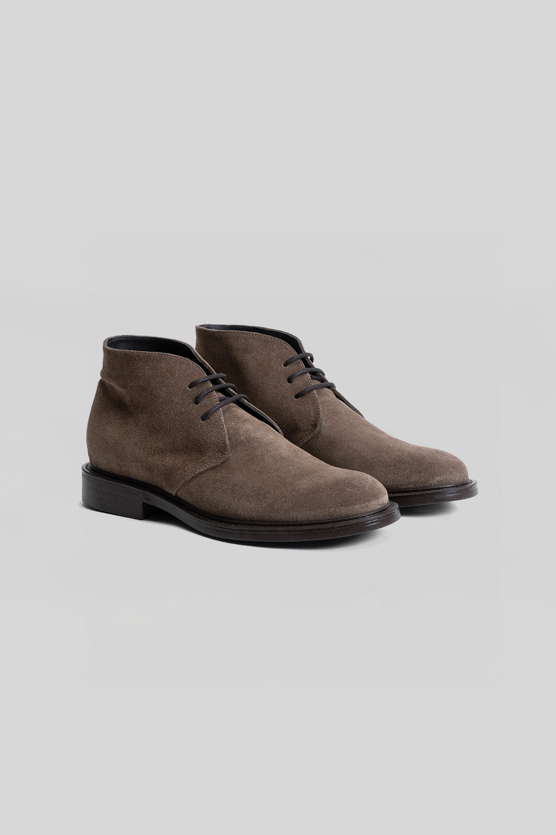 Brown suede chukka boots with black laces and black soles, shown as a pair from a three-quarter view.
