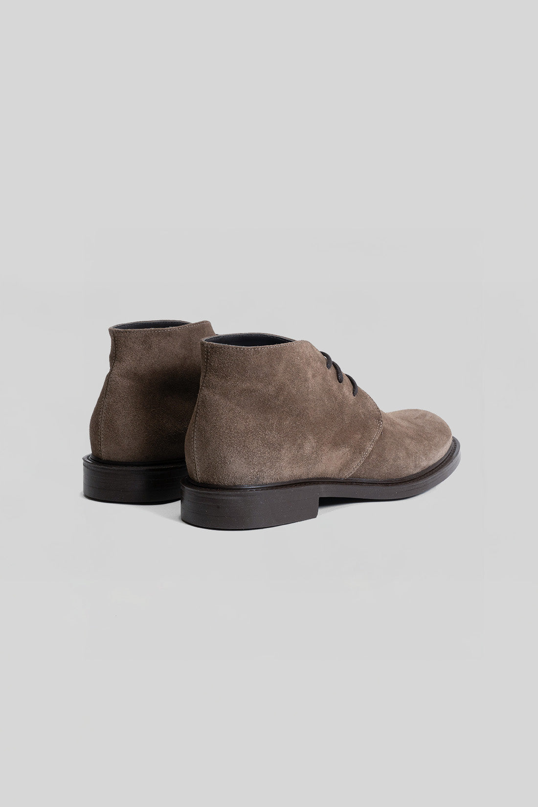 Brown suede chukka boots with black soles and lace-up closure, shown from the back.