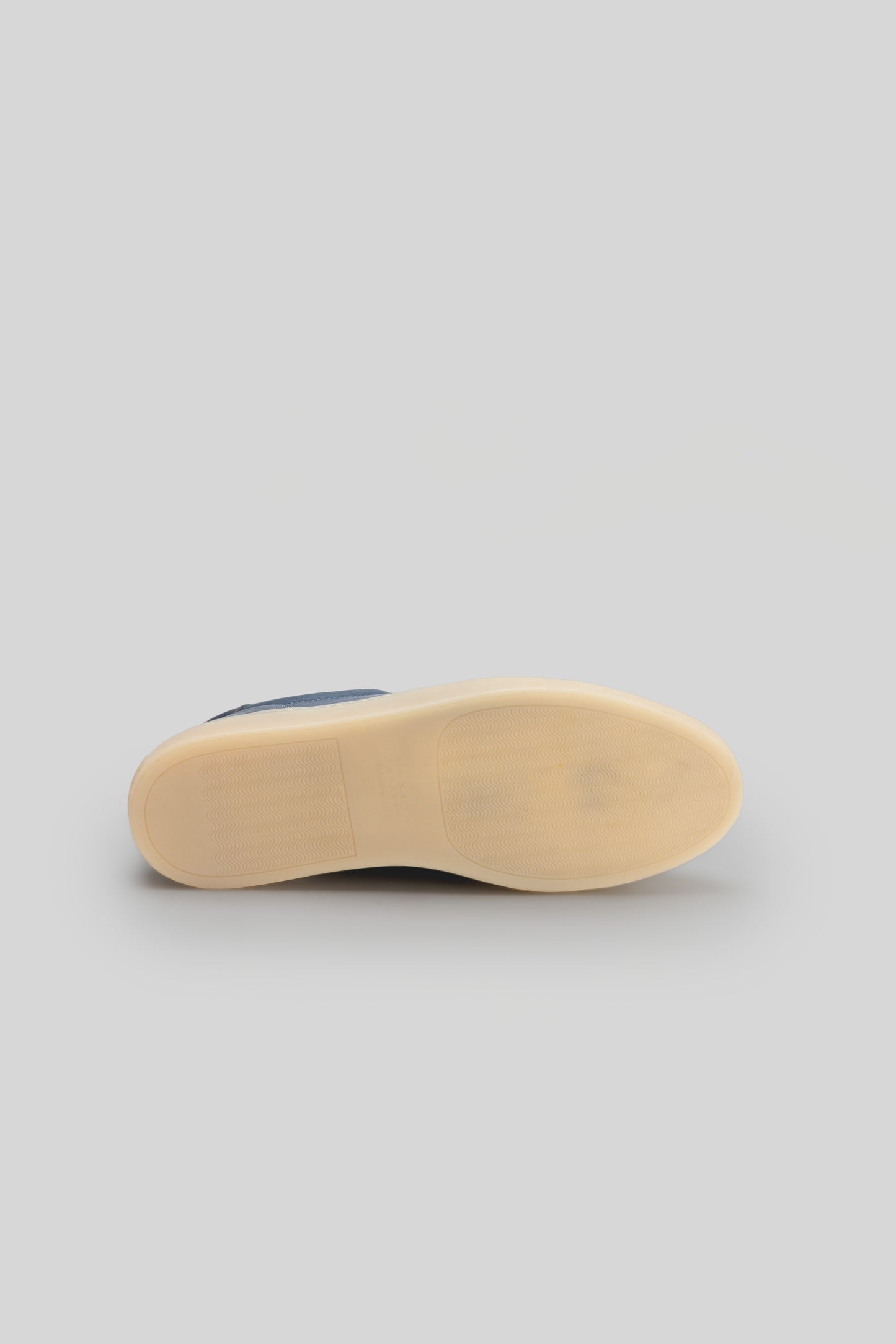 Cream rubber sole of a navy and cream leather sneaker shown from underneath.