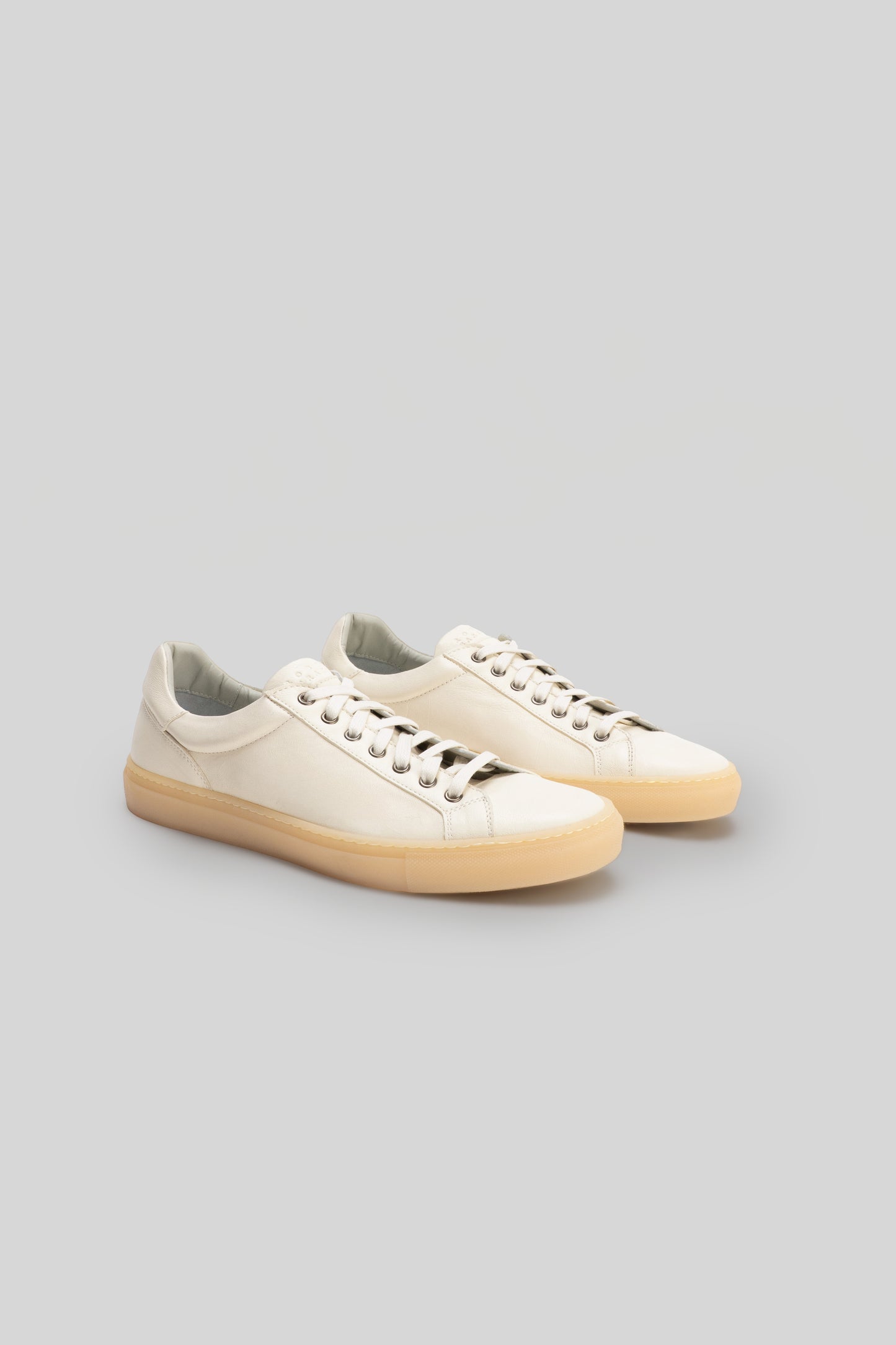 Pair of cream leather low-top sneakers with tan rubber soles and white laces, shown from a three-quarter angle.