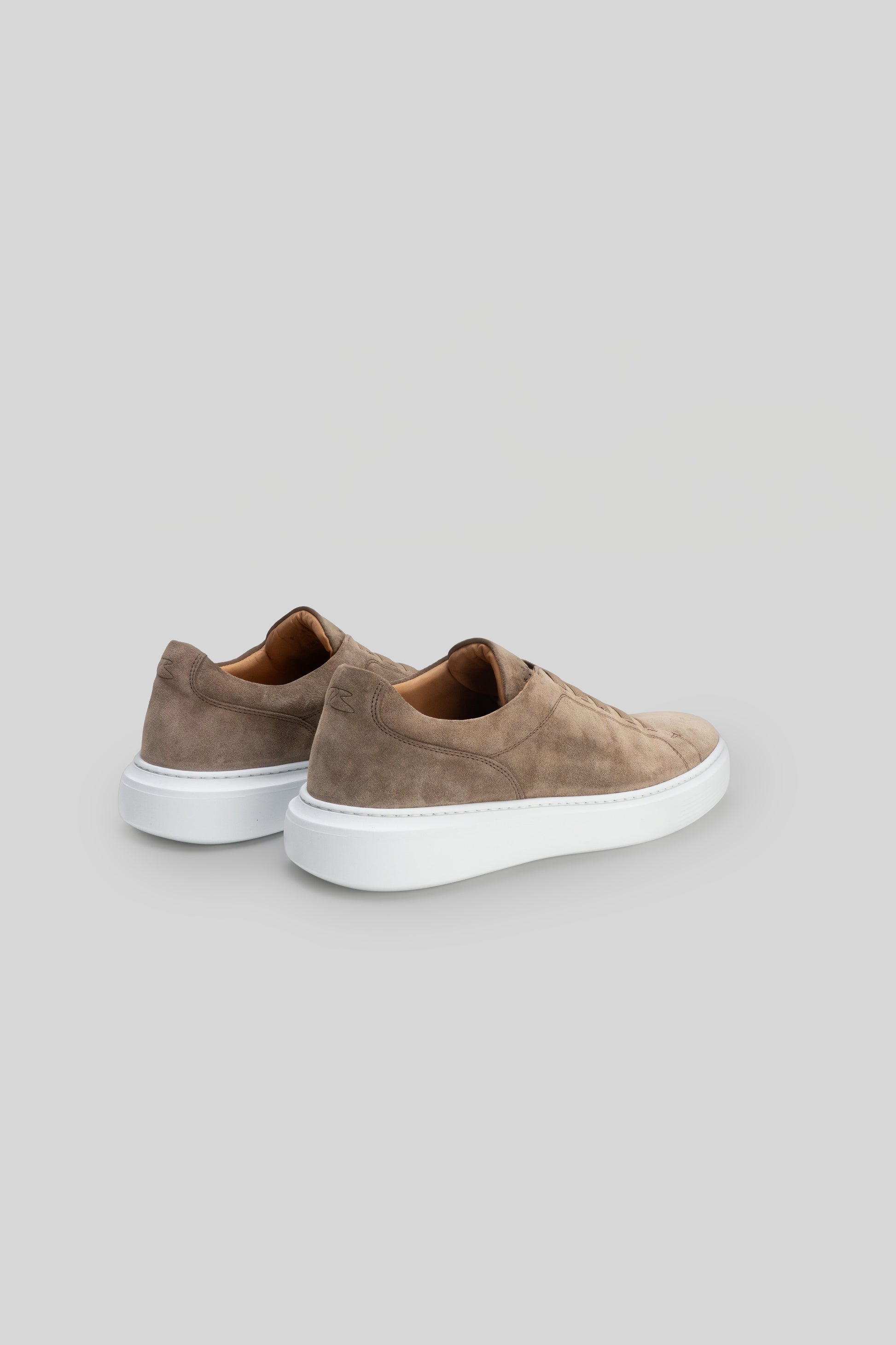 Pair of taupe suede slip-on sneakers with white rubber soles, shown from the back angle.