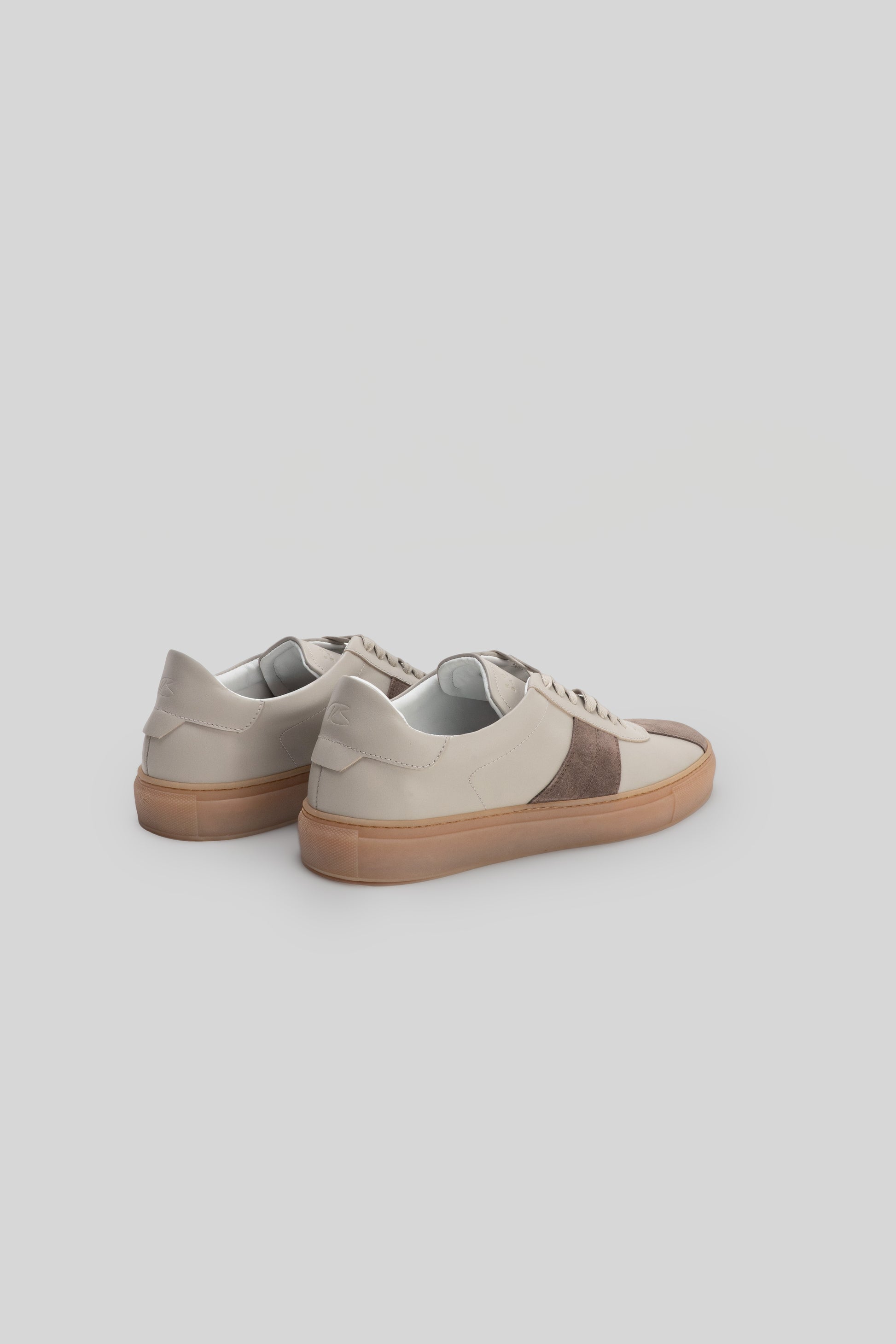 White and brown stripe sneaker with tan rubber sole, shown from rear three-quarter view.