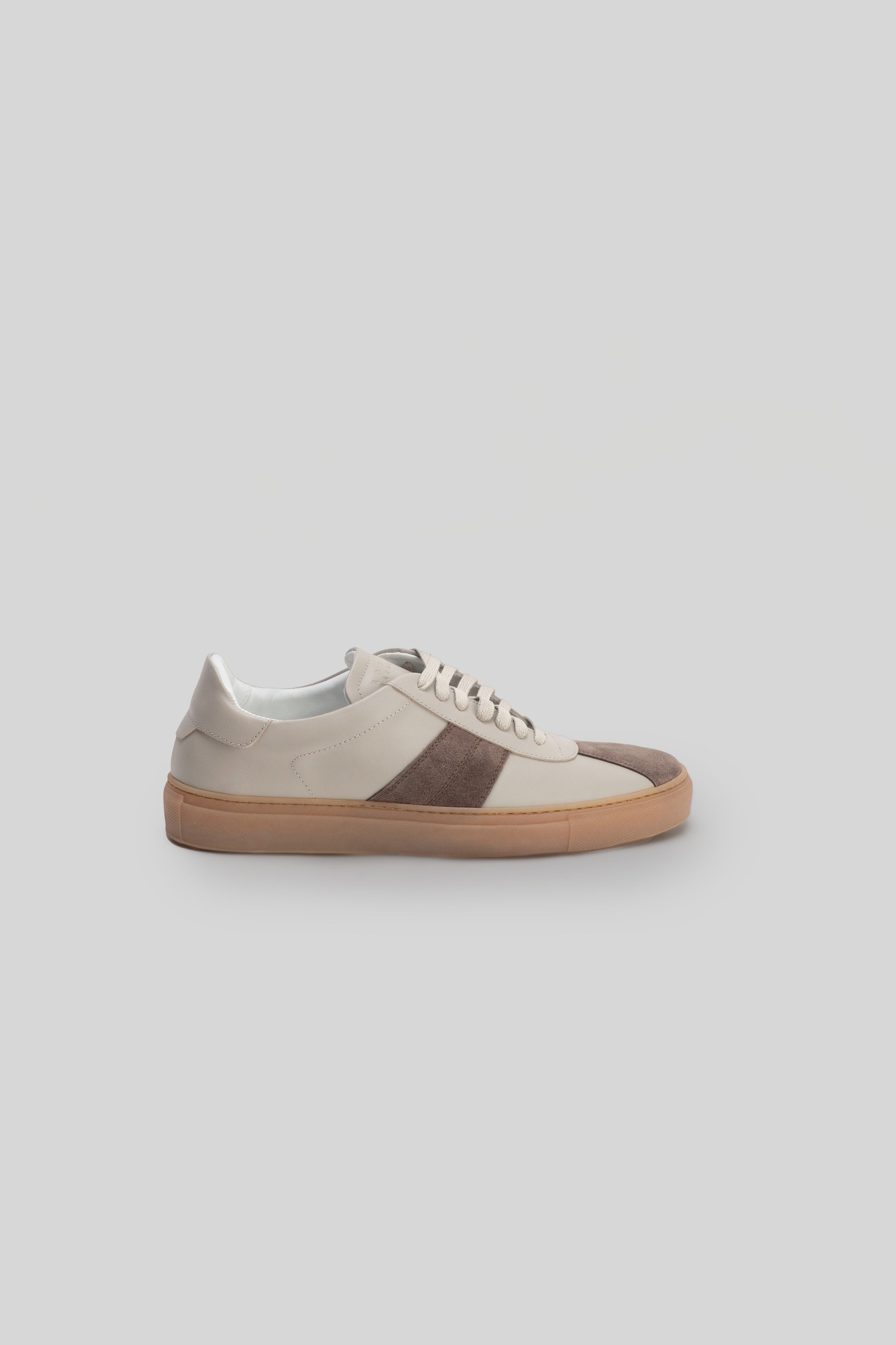 White sneaker with brown stripe detail across the side and tan rubber sole, shown in profile view.