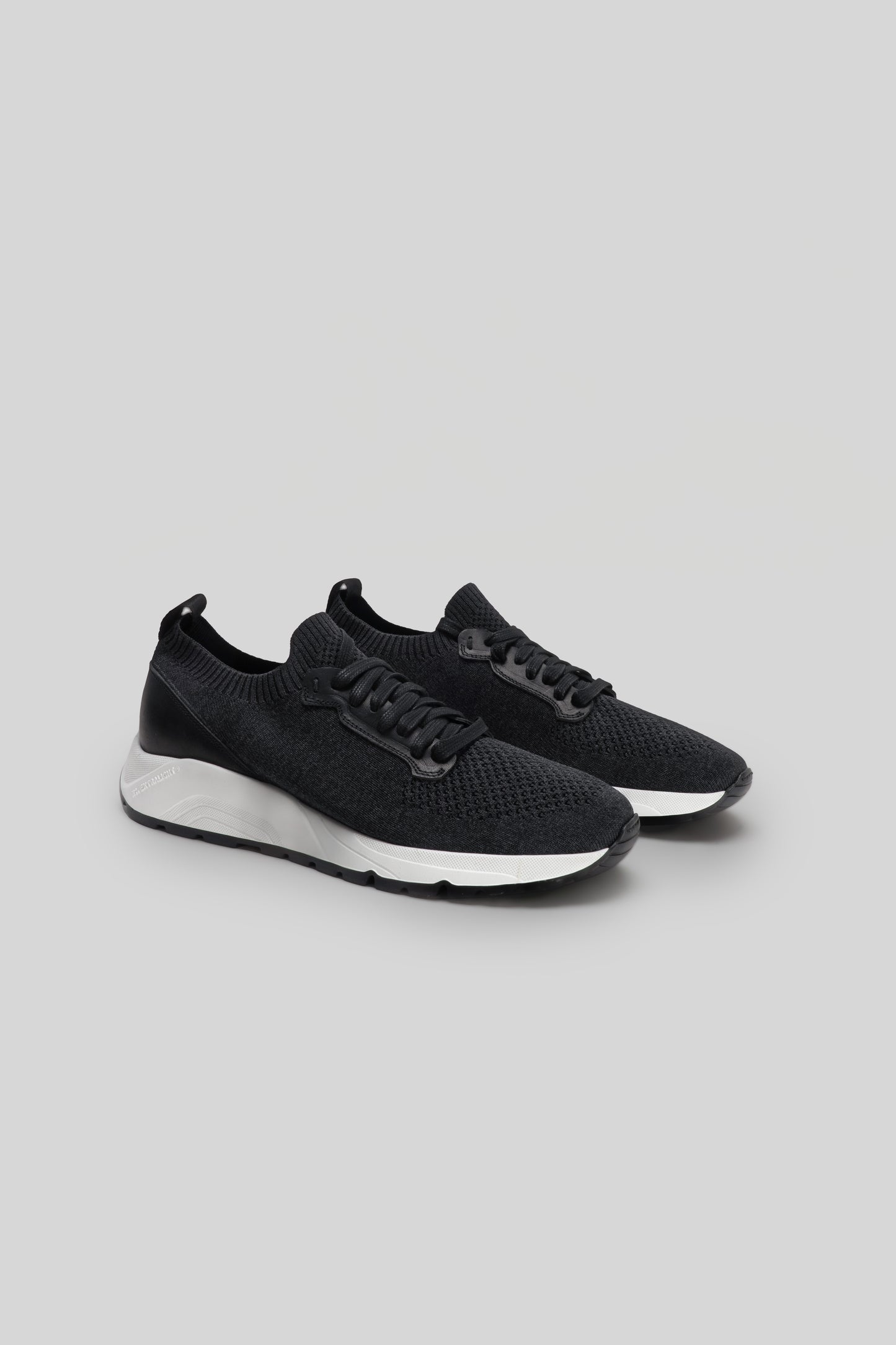 Black knit sneakers with white sole and black laces, shown from the side.