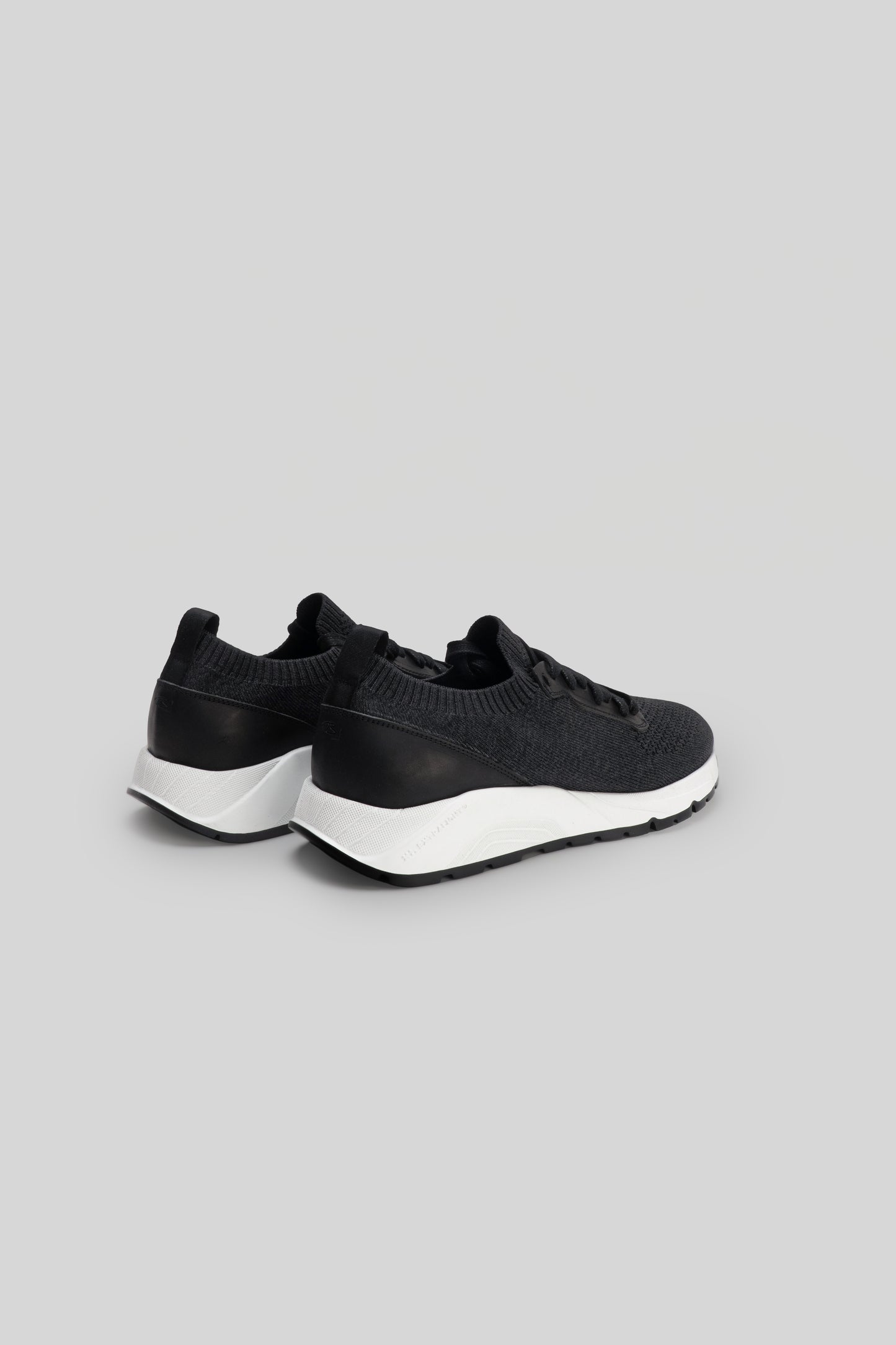 Black knit sneaker with white sole and black heel panel, shown from rear three-quarter view.