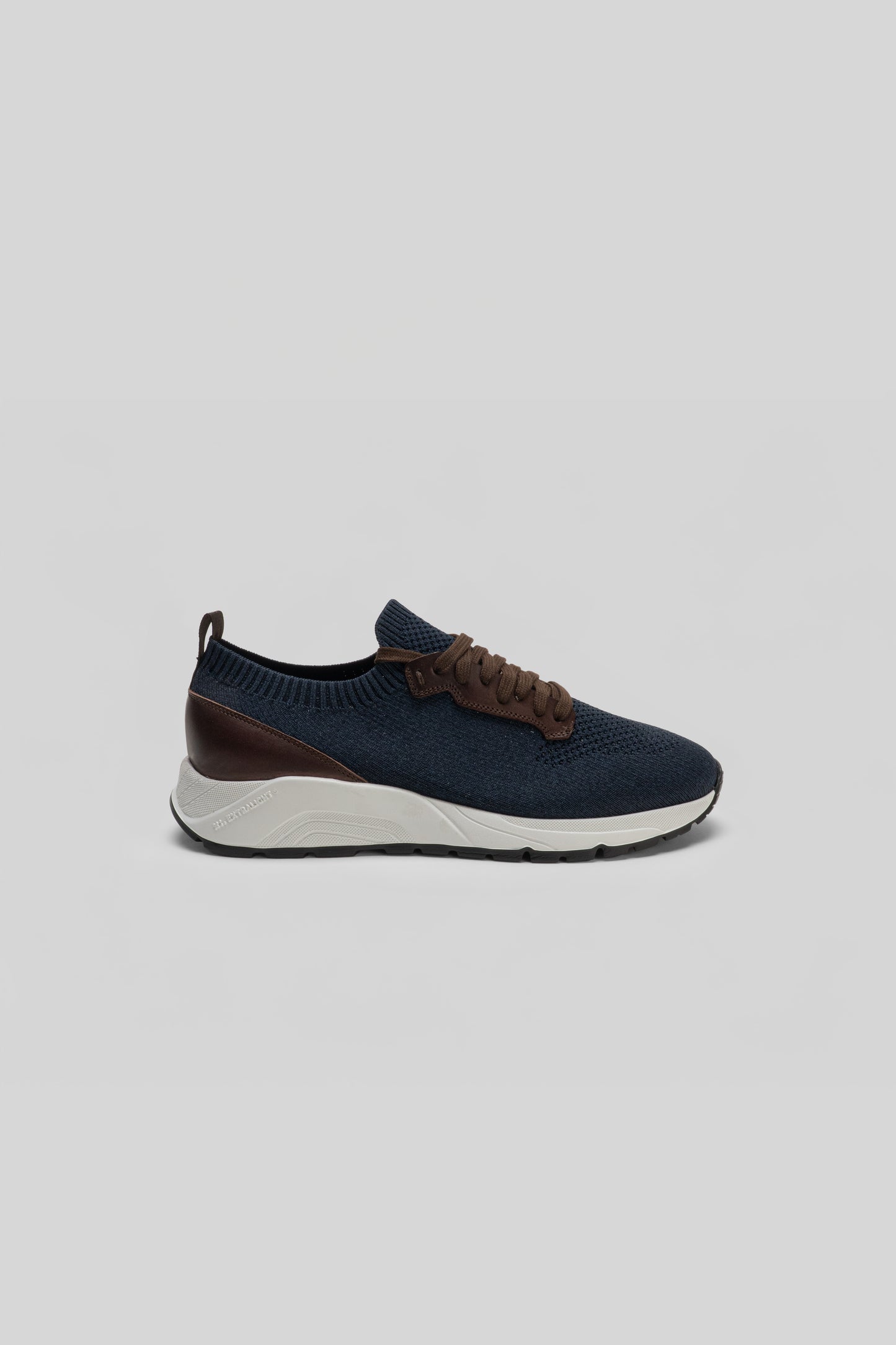 Navy knit sneaker with brown leather trim, white midsole, and black heel detail shown in profile view.