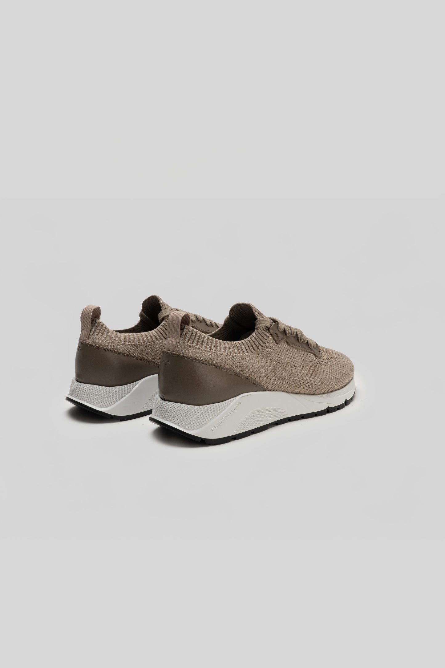Pair of beige knit sneakers with taupe heel panels and white midsoles, shown from rear three-quarter view.