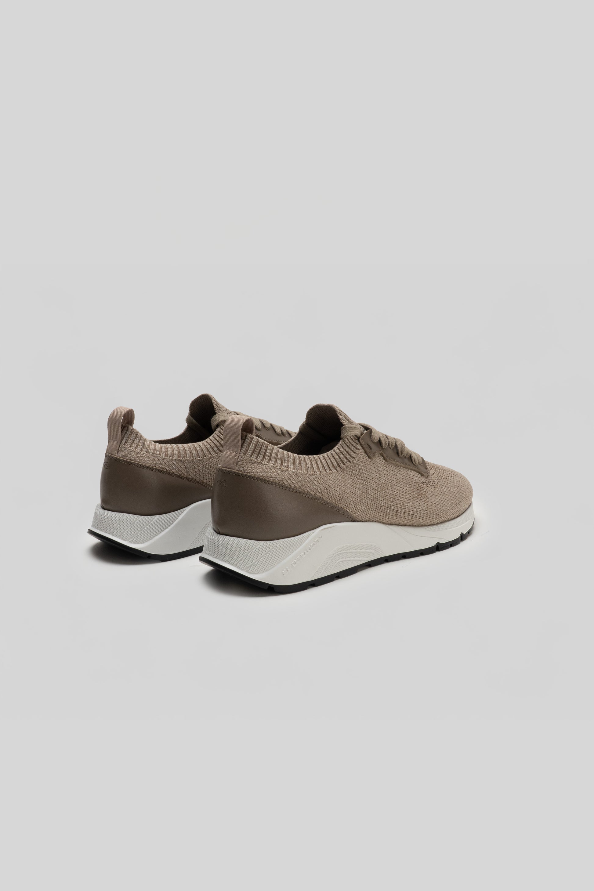 Pair of beige knit sneakers with taupe heel panels and white midsoles, shown from rear three-quarter view.