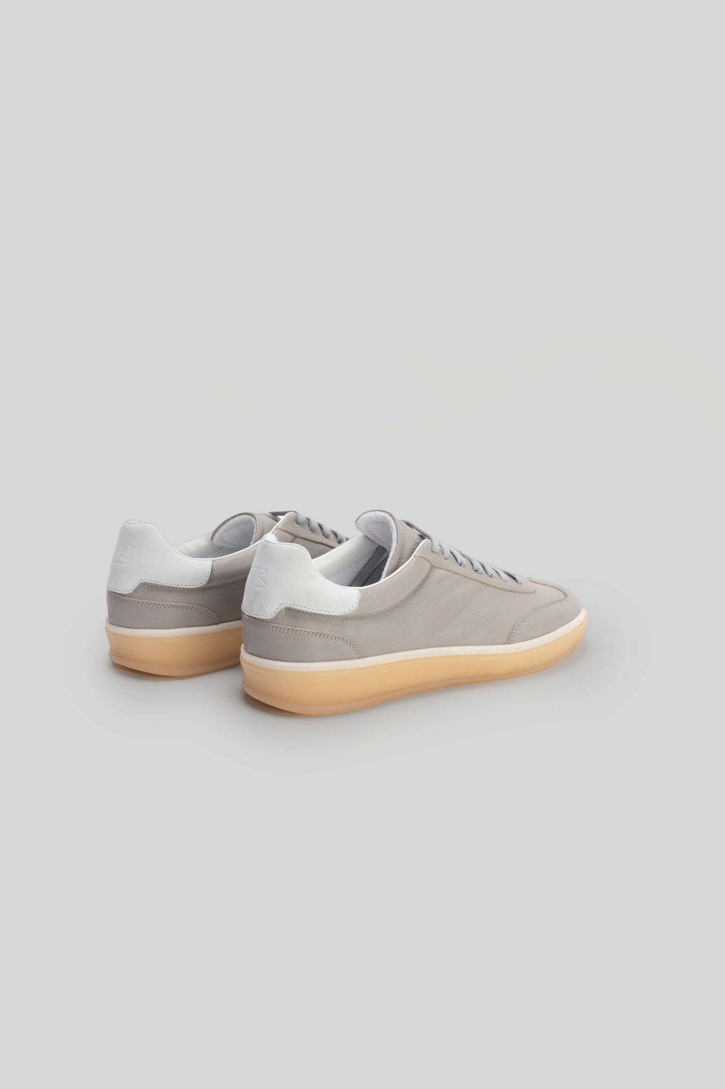 Beige and white lace-up sneaker with tan sole, shown from rear three-quarter view.