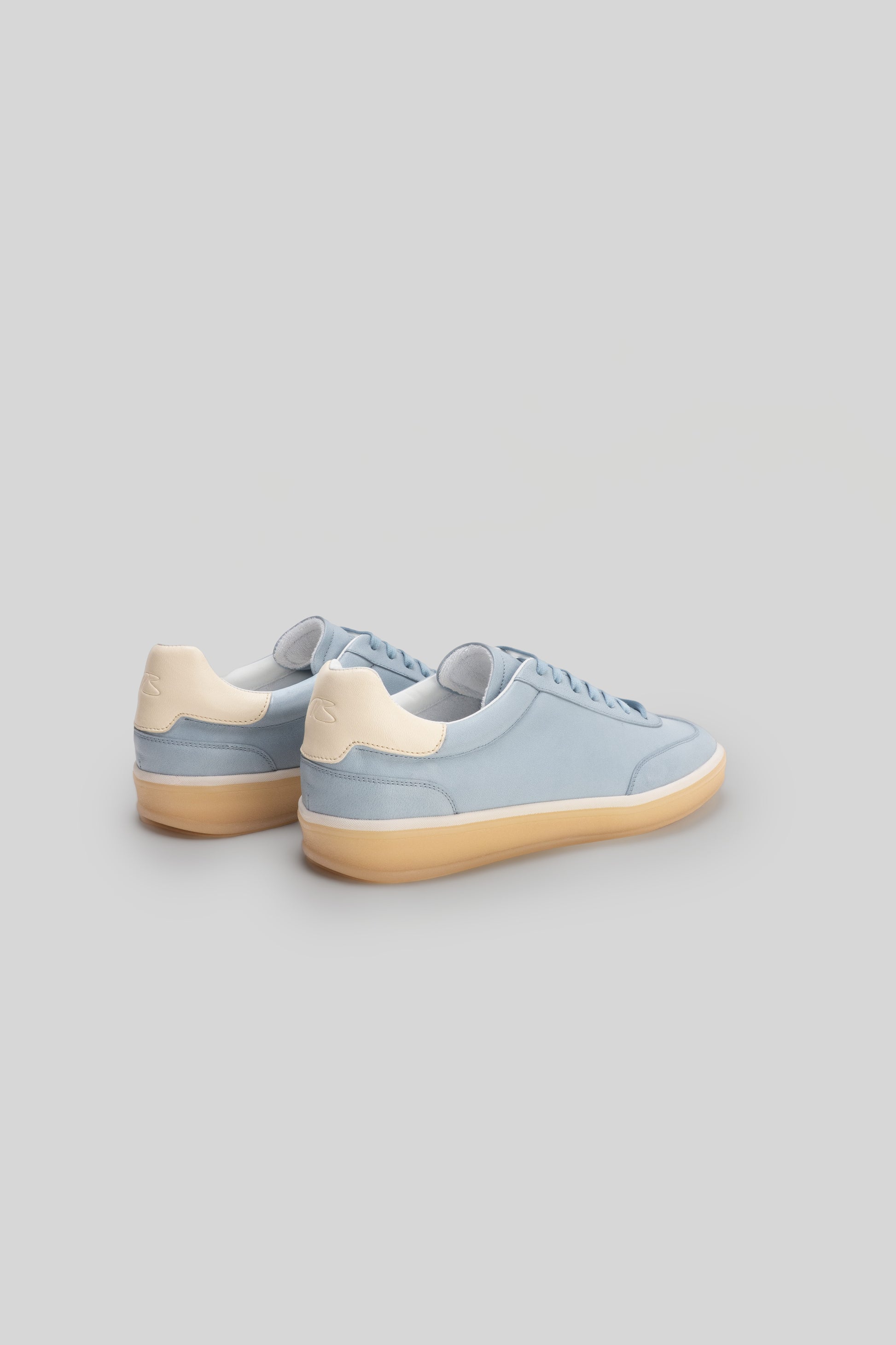 Light blue and cream lace-up sneakers with padded collar and tan rubber sole, shown from rear three-quarter view.