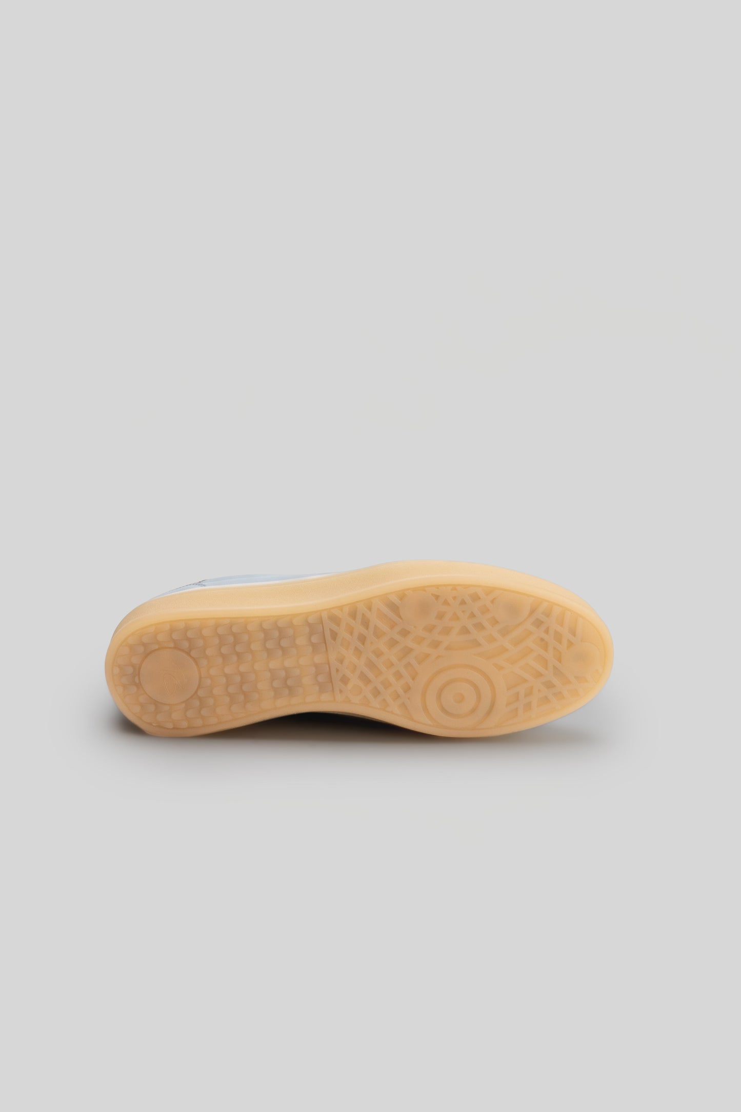 Sole view of white and tan sneaker with textured tread pattern and circular grip details.
