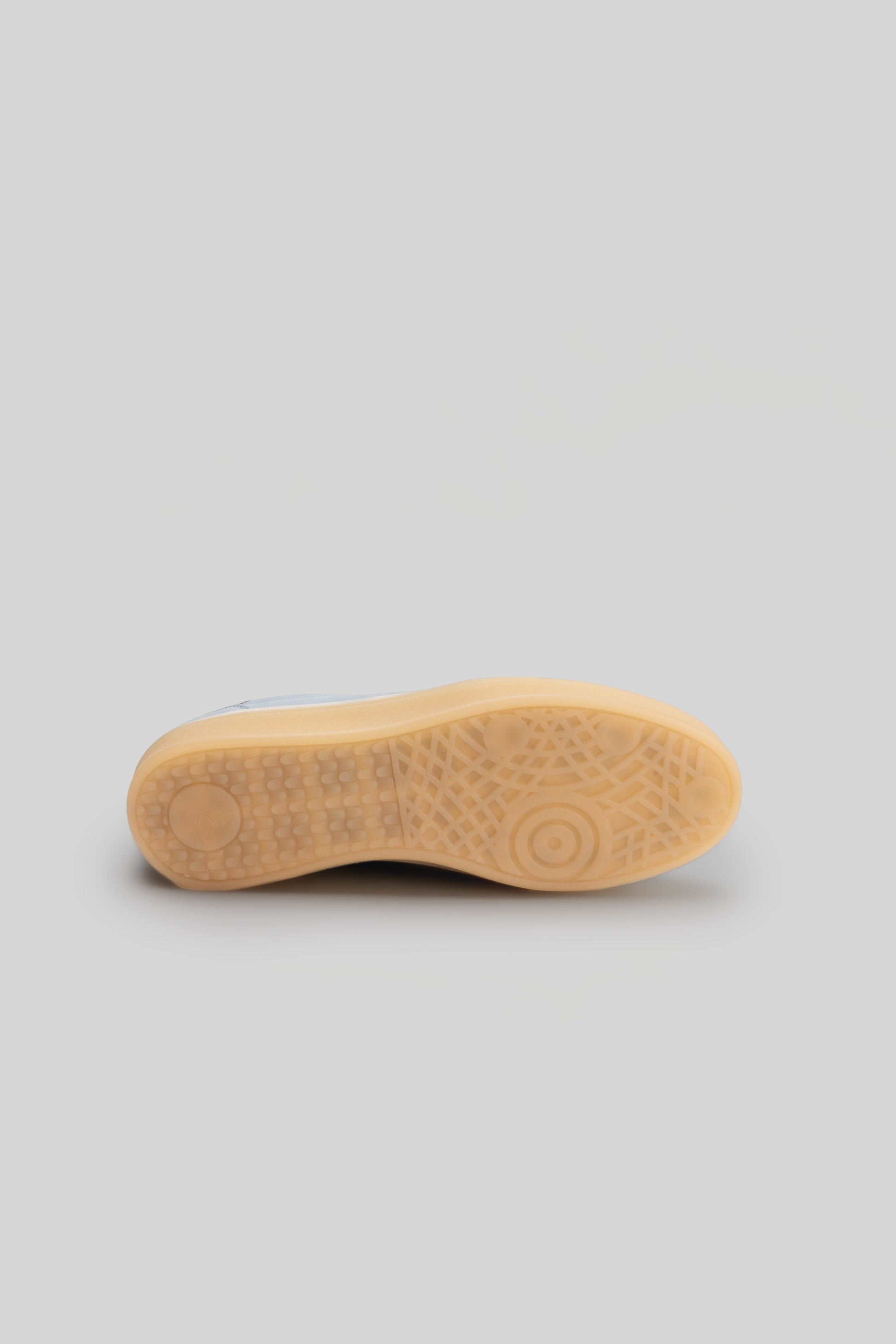 Sole view of white and tan sneaker with textured tread pattern and circular grip details.