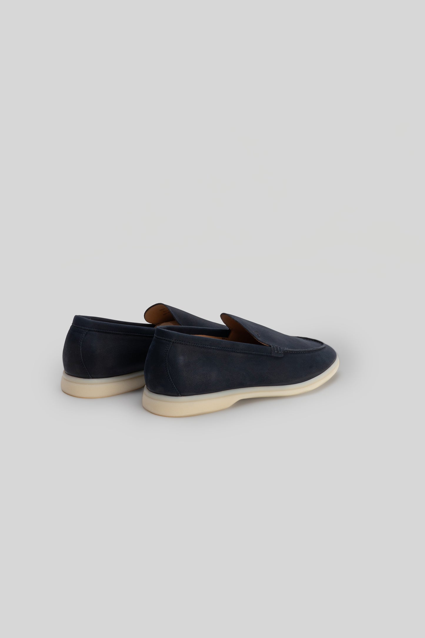 Navy suede loafers with cream crepe sole and brown leather interior lining, shown from rear three-quarter view.