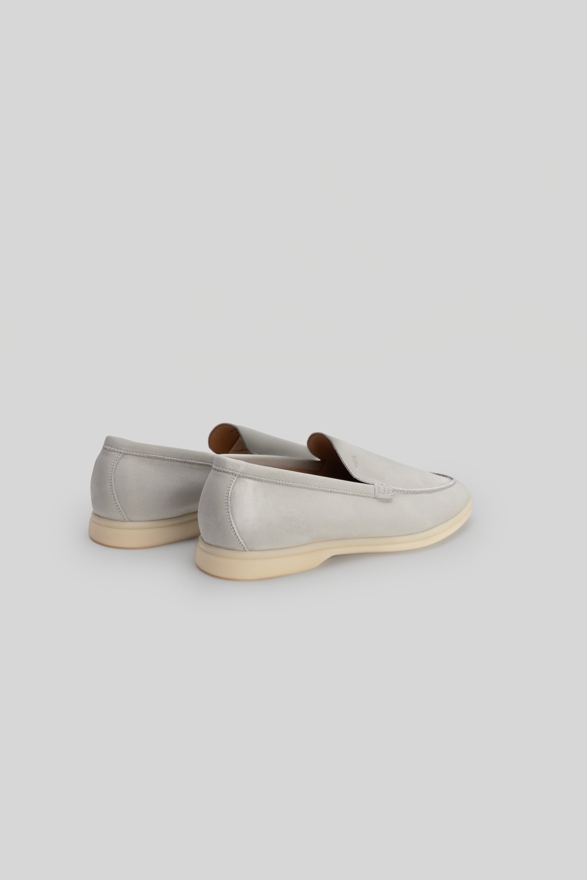 Pair of light gray suede loafers with crepe sole and brown leather interior, shown from rear three-quarter view.
