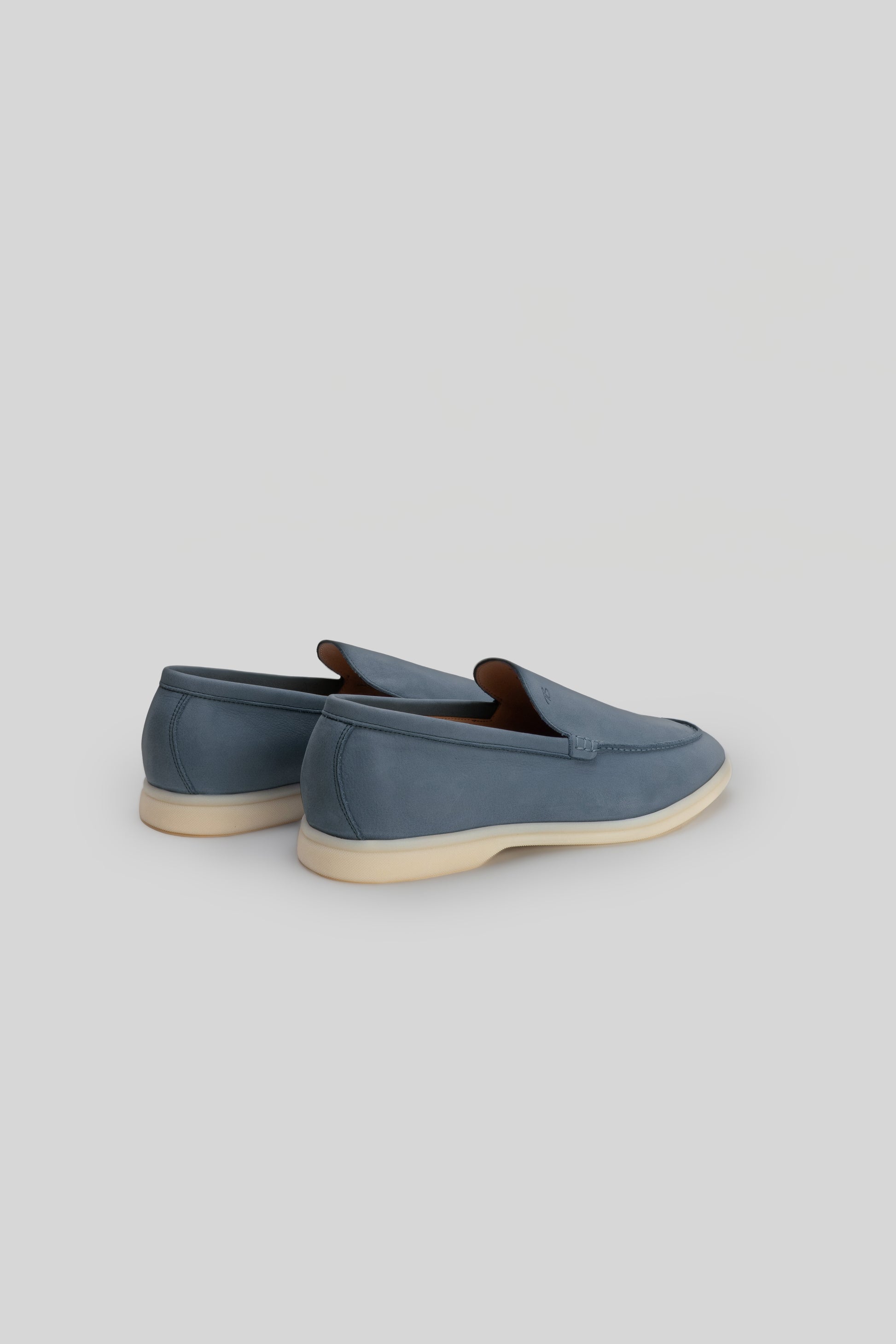 Blue suede loafers with brown leather trim and cream-colored crepe sole, shown from rear three-quarter view.