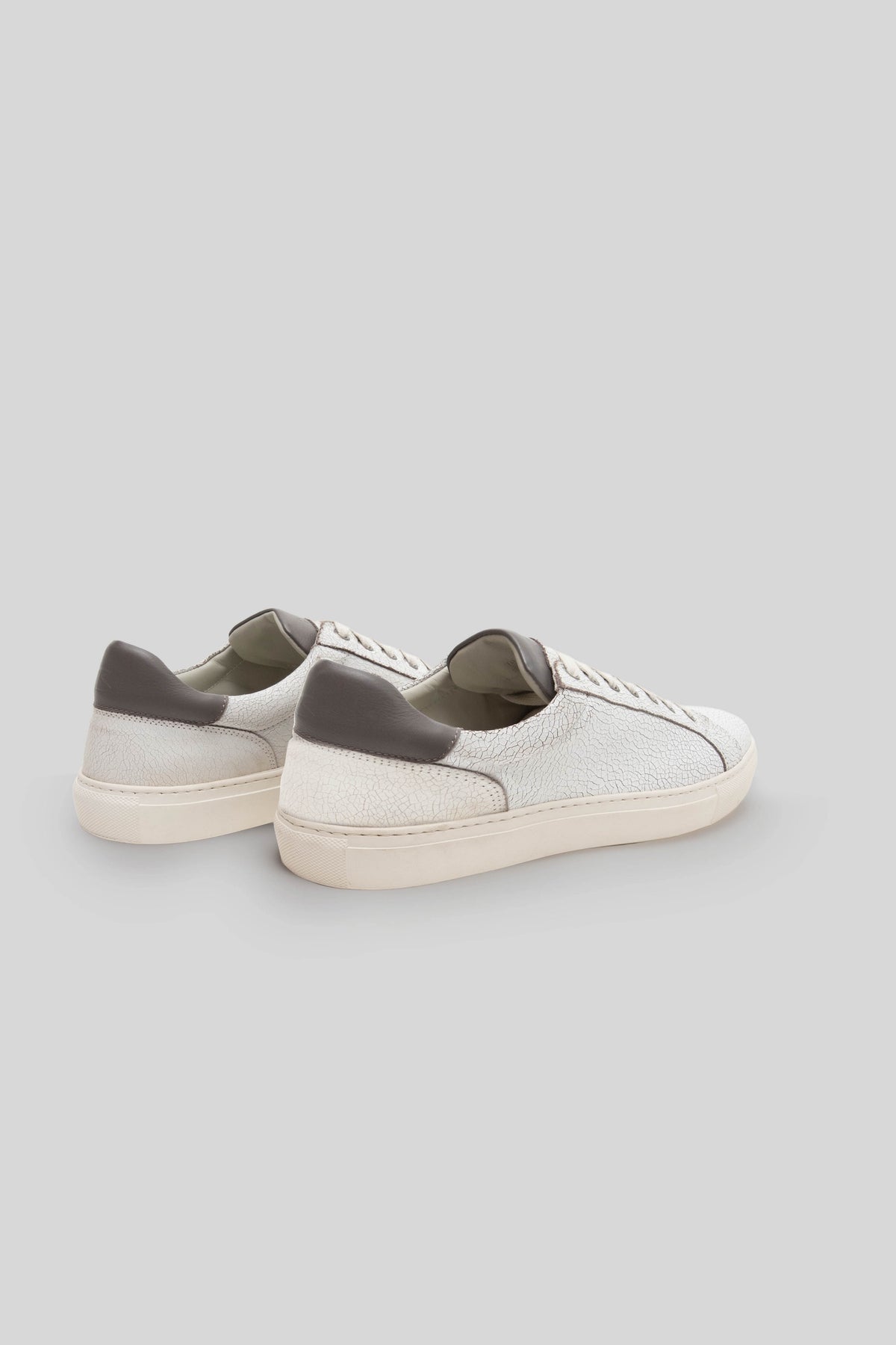 White leather sneakers with gray heel panels and cream-colored sole, shown from rear three-quarter view.
