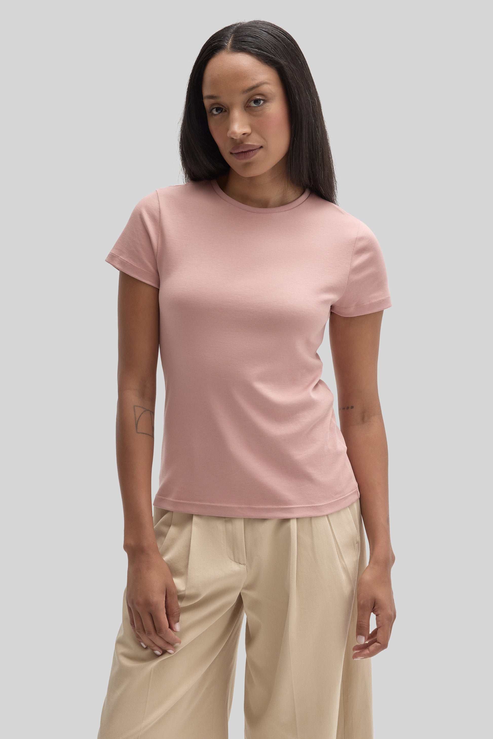 Woman wearing a dusty pink crew neck t-shirt with short sleeves and beige pants.