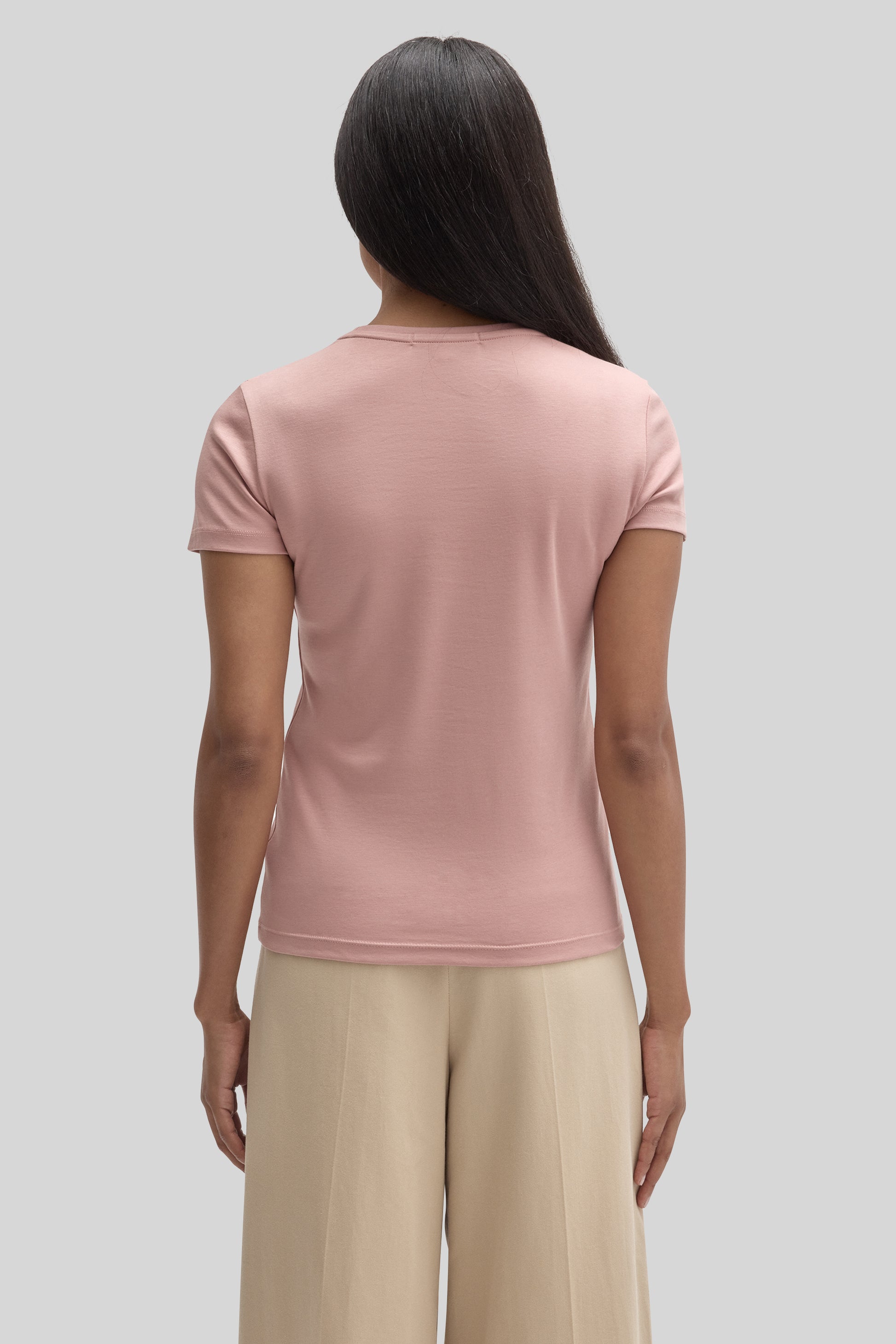 Woman wearing a dusty pink short-sleeve crew neck tee paired with cream-colored trousers, shown from behind.