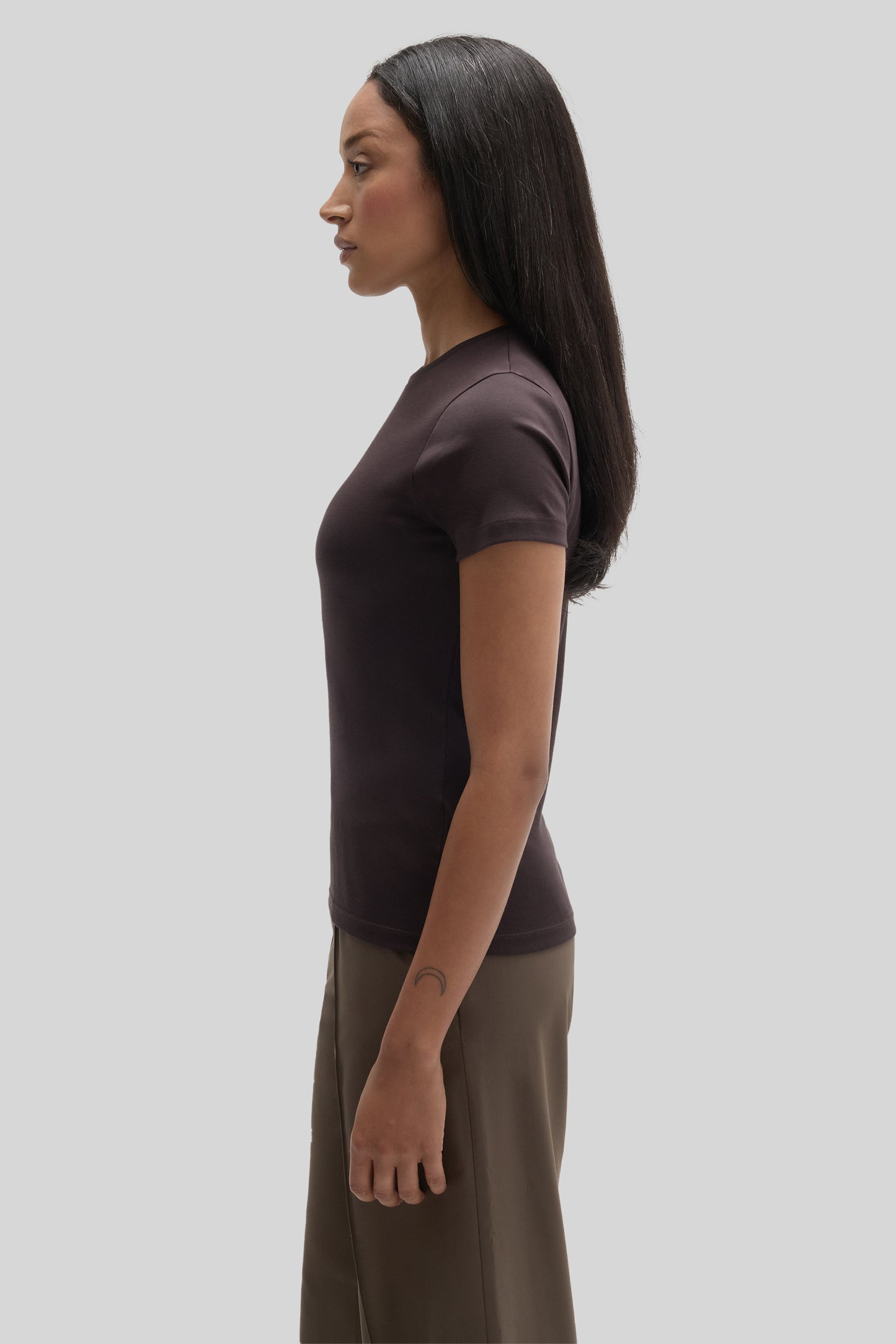 Woman wearing a dark brown short-sleeve fitted tee with khaki pants, shown from the side.