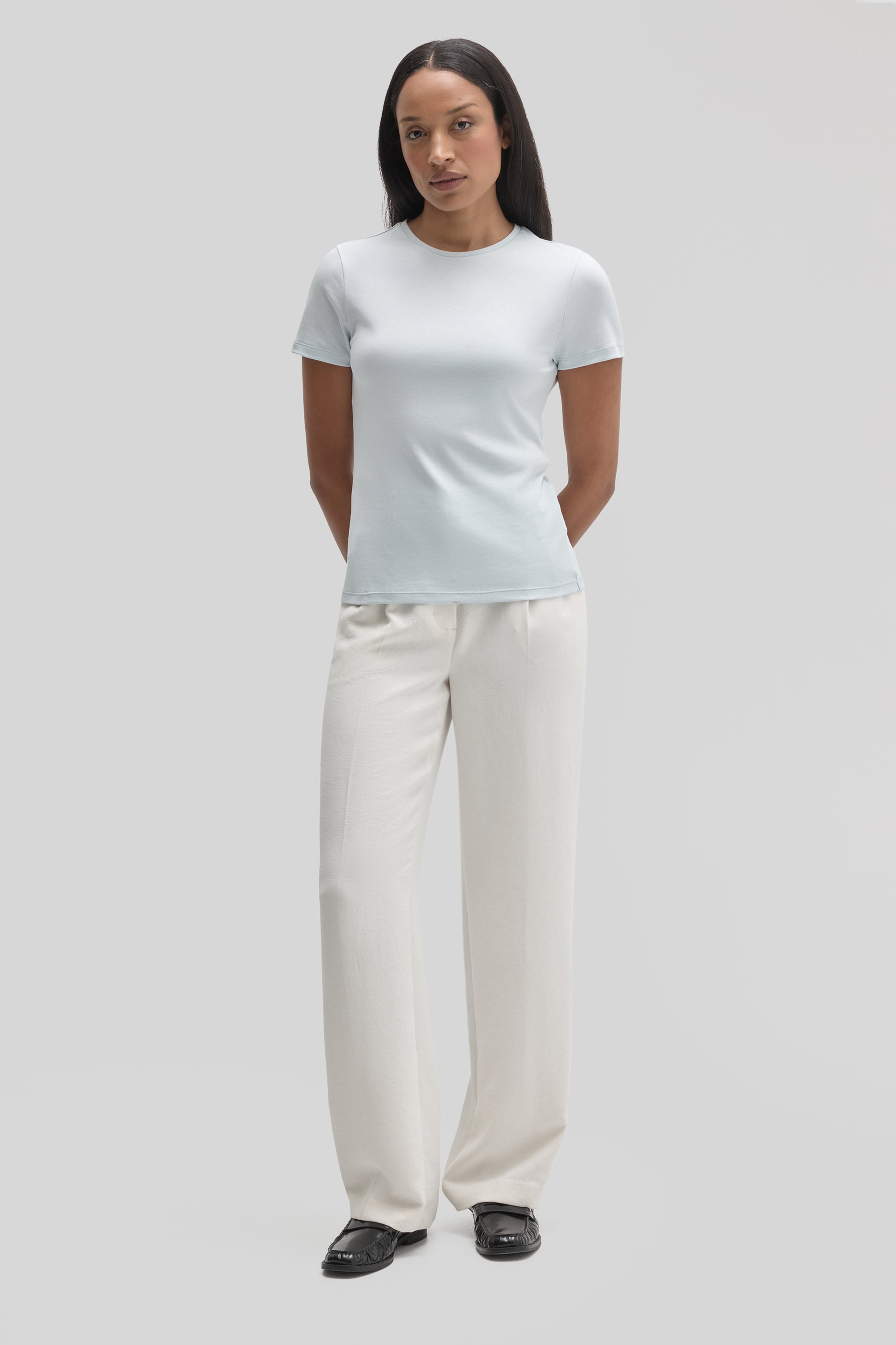 Woman wearing white short-sleeve crewneck tee with cream pants and black slides.