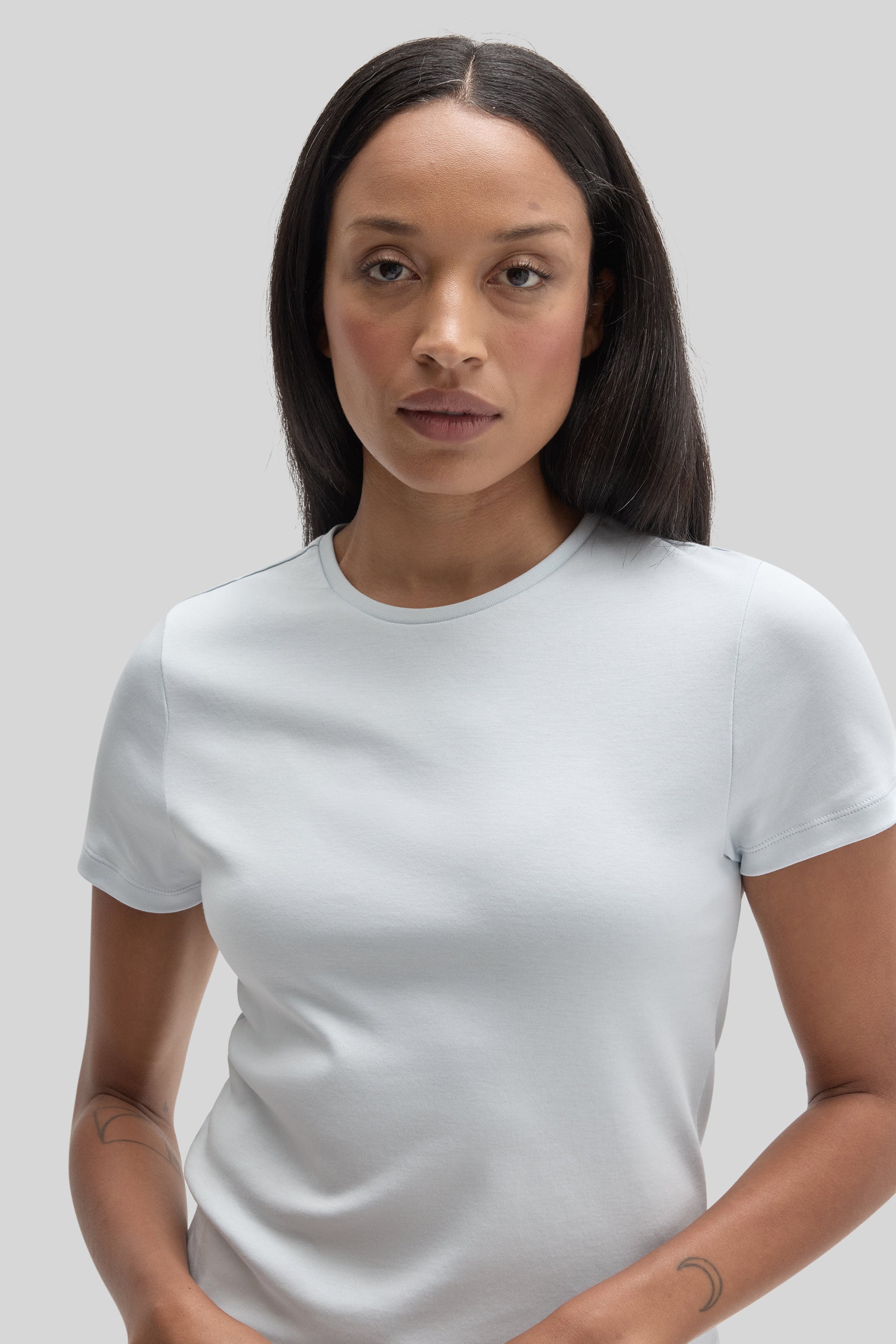 Woman wearing a white crewneck short-sleeve t-shirt against a neutral background.