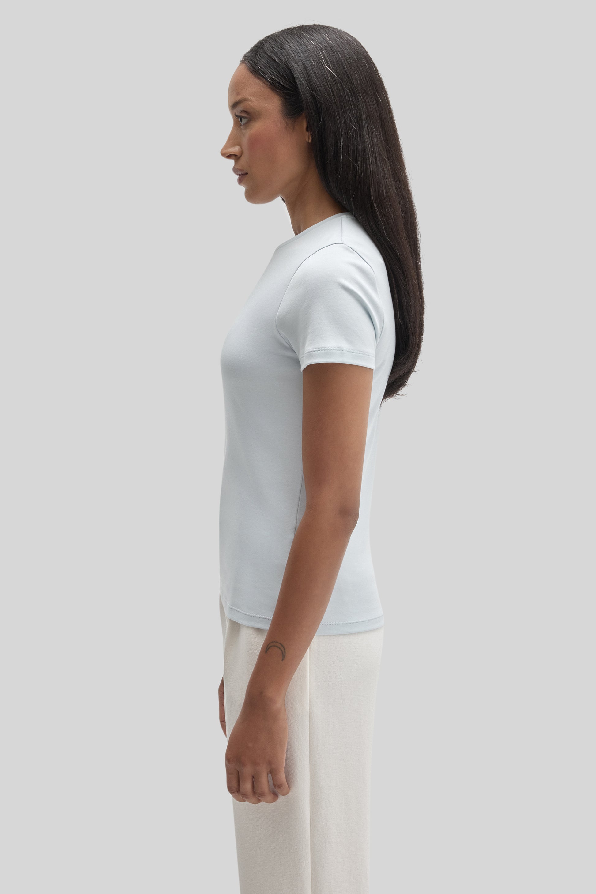 Woman wearing white short-sleeve fitted t-shirt with cream-colored pants, shown in side profile.