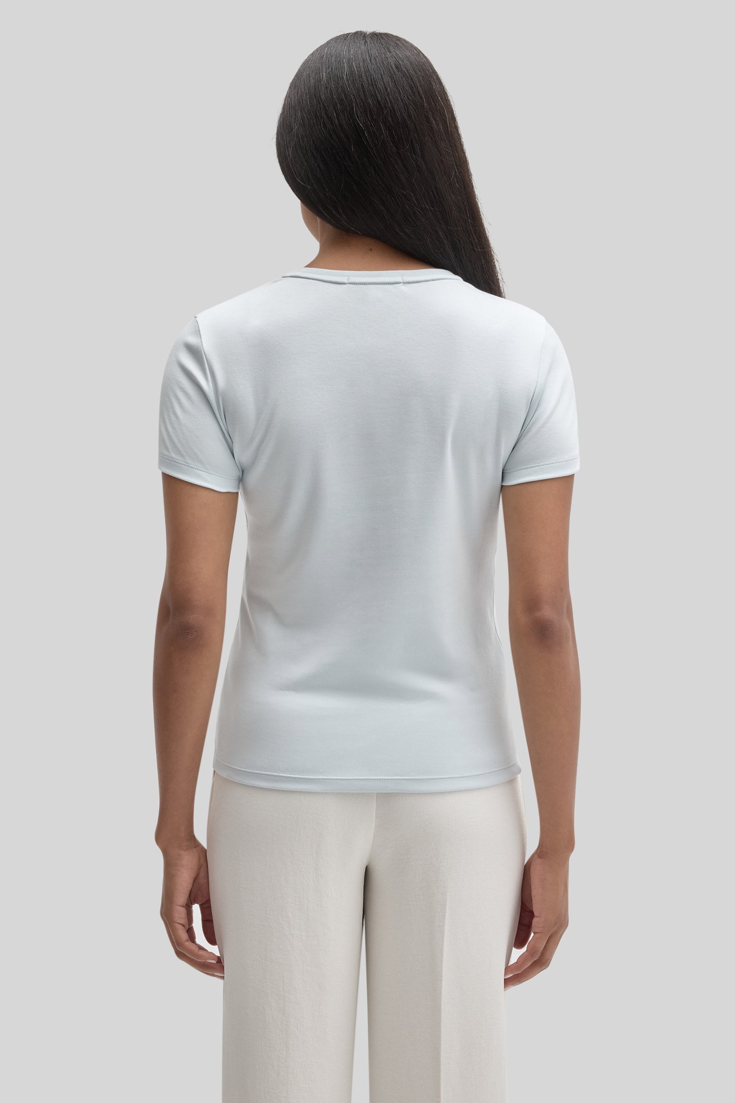 Woman wearing white short-sleeve crew neck tee, shown from back view.