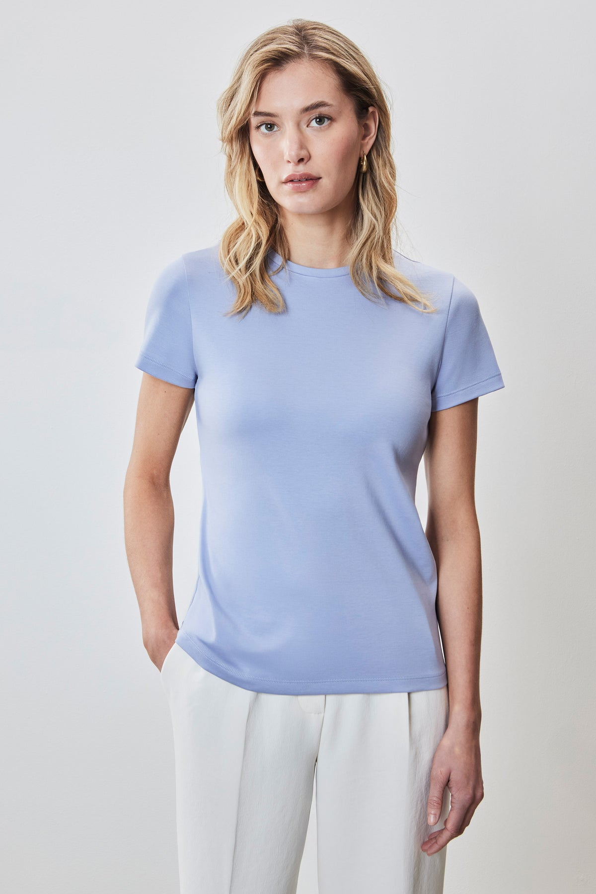 Woman wearing a light blue crew-neck t-shirt with short sleeves and white pants.