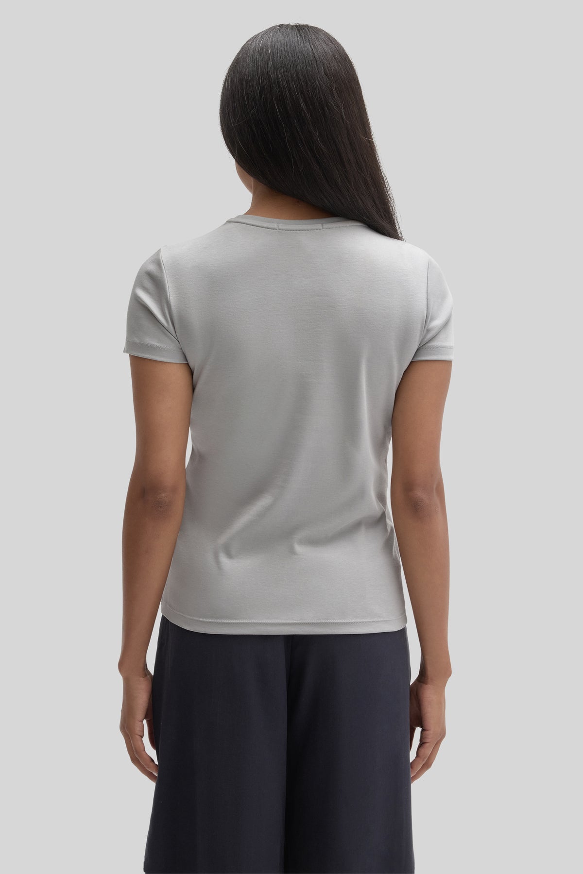 Woman wearing light gray short-sleeve t-shirt and dark pants, shown from behind.