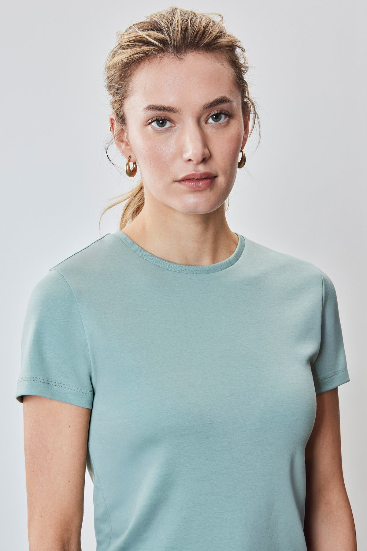 Woman wearing a sage green crewneck short-sleeve tee.
