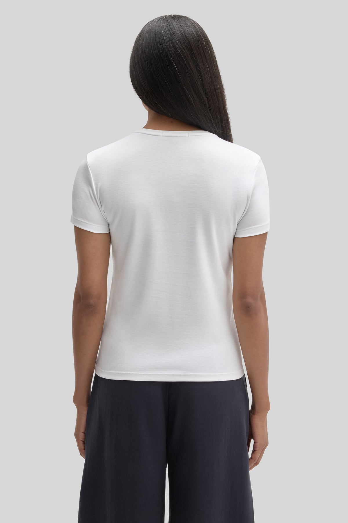 Woman wearing white short-sleeve t-shirt with crew neckline, shown from back view.